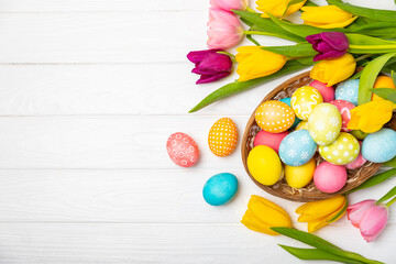 Obraz na płótnie Canvas Easter basket filled with colorful eggs and a bouquet of tulips on a textured wooden table. Easter celebration concept. Colorful easter handmade decorated Easter eggs. Place for text. Copy space