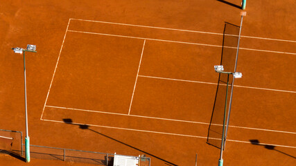 Aerial closeup of a red clay tennis court. The sports center is empty and there is no one on the...