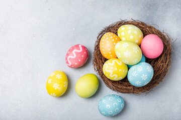 Easter eggs in the nest with mimosa flowers on a bright background. Easter celebration concept. Colorful easter handmade decorated Easter eggs. Place for text. Copy space.
