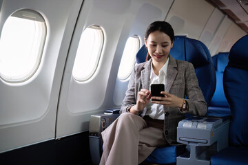 Young Asian woman checks business news on mobile phone, sitting near window in first class on...
