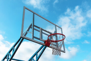 Red basketball hoop with a glass backboard against a blue sky © Klochkov