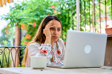 portrait of a young woman working on her laptop with a troubled look on her face