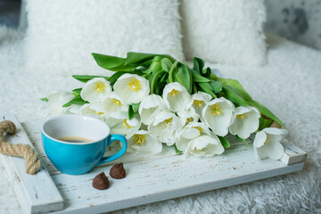 white tulip flowers, a cup of coffee and chocolate truffles on a white tray in bed.
