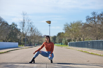 Fototapeta premium Young and beautiful brunette woman with short hair, dressed in jeans and orange shirt is bent over with one leg stretched out and the other bent.