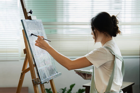 beautiful young woman artist working on painting something on a large canvas