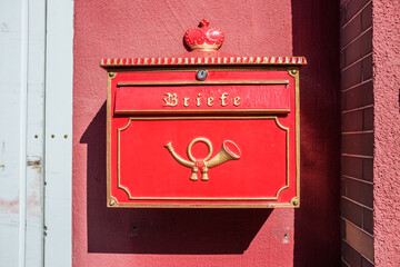 Roter Briefkasten mit goldener Krone und goldenem Posthorn an roter Hauswand