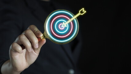 Hand holding magnifier glass with dartboard with arrow for focus and setup business objective target and goal concept.