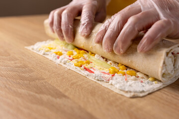 Lavash with filling and vegetables is wrapped in a roll. Preparation of pita bread roll.