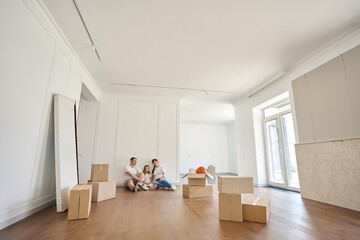 Fototapeta premium Serious caucasian family on floor looking at new modern townhouse during moving
