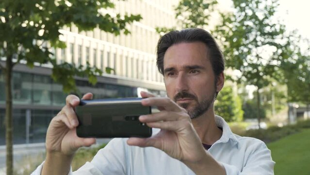 A handsome Caucasian man takes pictures with a smartphone in an urban area - closeup