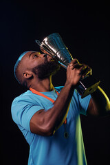 Vertical portrait of African American sportsman kissing trophy cup and celebrating victory