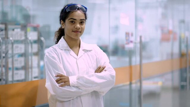 mujer joven afroamericana en guardapolvo y bata blanca en pasadizo frente a laboratorio