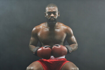 Fototapeta na wymiar Front view portrait of tough African American boxer wearing red gloves and looking at camera sitting against black background