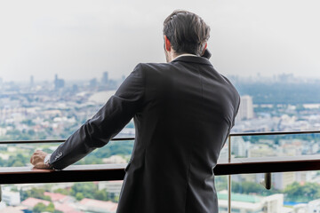 Fototapeta premium Portrait back view businessman talking on smartphone looking at city view from high rise office balcony