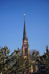 Blick über alte Planeten am Mainufer auf den spitzen Kirchturm der Dreikönigskirche vor blauem Himmel im Sonnenschein im Stadtteil Sachsenhausen in Frankfurt am Main in Hessen