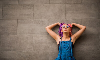 mujer joven latina con los brazos en la cabeza recostada en muro gris 