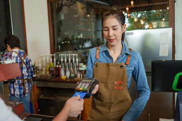 Young Asian business owner, cafe owner Using a card swiping machine to charge customers at the...