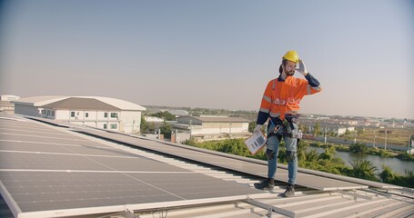 A solar panel technician engineer in safety harness and hard hat inspects a rooftop solar...
