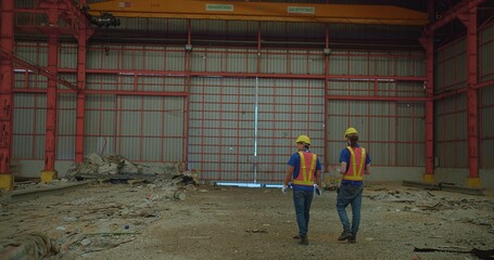 Two construction workers in yellow hard hats and reflective vests discussing stand amidst a large...