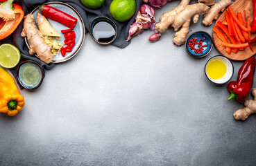Food and cooking background with fresh raw vegetables. Gray table with paprika, zucchini, spices and ingredients for cooking Asian dishes with ginger, garlic, soy sauce and lime, top view