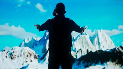 Man wearing virtual reality glasses stands in front of big digital screen playing moving mountains, cyber visual background, back shot. © kinomaster