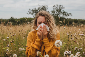 female person in a field blowing her nose, person with allergies standing in a field, person with pollen allergy blowing his nose 