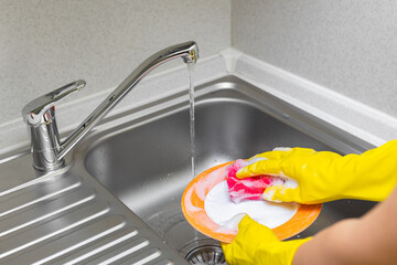 housewife in rubber gloves washes dishes in the kitchen.