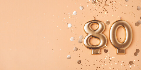 80 years celebration. Greeting banner. Gold candles in the form of number eighty on peach background with confetti.