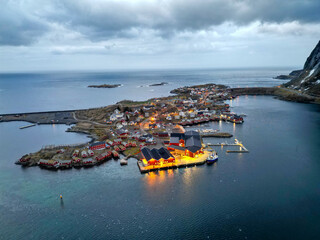 Dusk falls over a remote fishing village in the Arctic, with warm lights illuminating the coastal...