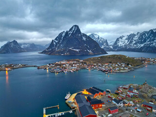 Aerial view of Lofoten island Norway. The winter season of sunrise fishing village of Reine with snowscape mountain peak reflect on water. Norway with red rorbu houses. With falling snow in winter.