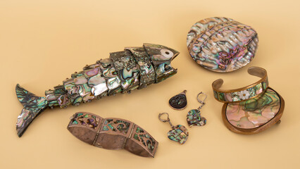 Jewelry and decorative fish made from abalone. Isolated objects on a light-yellow background....