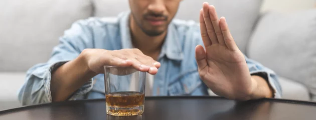 Fotobehang Alcoholism, depressed asian young man refuse, push out alcoholic beverage glass, drink whiskey, sitting alone at night. Treatment of alcohol addiction, having suffer abuse problem alcoholism concept. © KMPZZZ