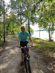 A young blonde woman rides a bicycle through the forest. Front view. Tourism, sports and outdoor recreation