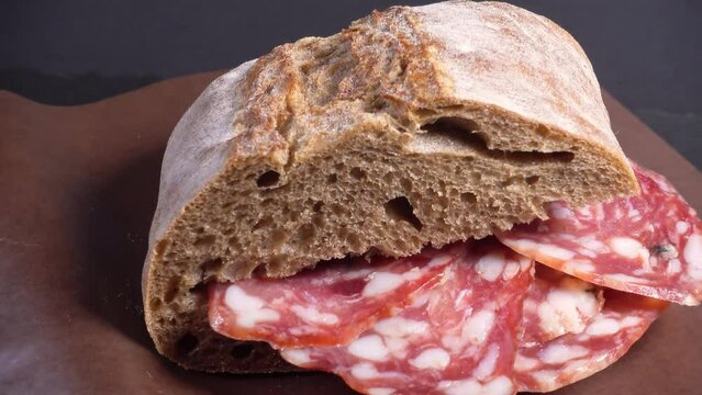 fresh crusty ciabatta bread with sliced salami, on paper, rotating