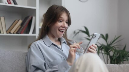 Portrait of young caucasian woman scrolling on smartphone while find incredible news promotion sale and extremely happy sitting on couch at home Advise Approve Recommend Choice concept