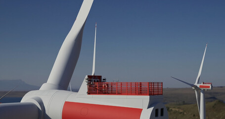 Large wind turbine rotating blades . Engineer performing repairing and maintenance works on top of wind turbine nacelle house. - obrazy, fototapety, plakaty