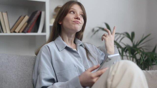 Pretty creative young woman student or freelancer thinks questioningly about difficult choice choose imagine plan in mind has doubts create idea sitting on couch with smartphone at home