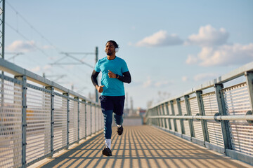 Black sportsman listening music on headphones while jogging outdoors.