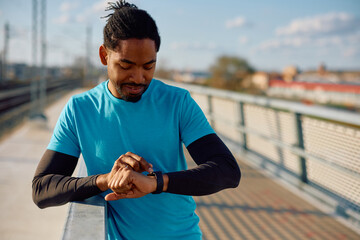 Black athletic man using smart watch while working out outdoors.