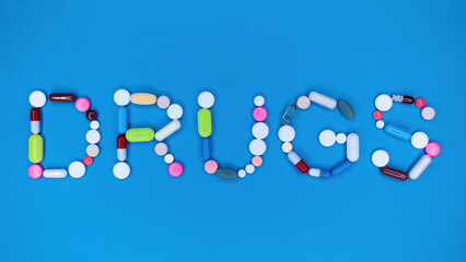Multicolored capsules in word drugs. Blue background. Pharmacy, antidepressants, medicine concept.