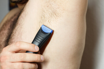 Male depilation. man using trimmer to remove hair from his armpit