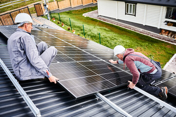 Mounters building photovoltaic solar module station on roof of house. Men electricians in helmets...