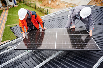 Electricians installing solar panel system on roof of house. Men workers in helmets carrying...