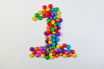 Colorful candies in the shape of the number 1 on white background