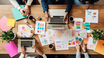 Close-up of a busy brainstorming session with multiple people, colorful note stickers, documents and laptops.