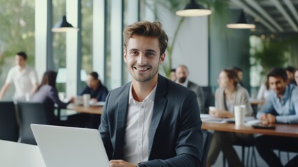 A man in a suit is smiling and sitting in front of a laptop
