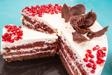 Red velvet cake with pomegranate seeds, sliced on a black ceramic plate, on a  table, soft focus...