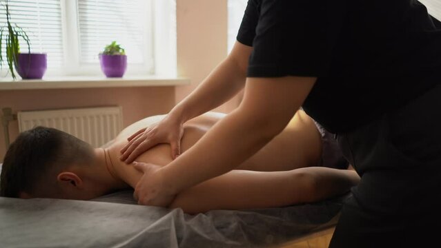 a young handsome sexy man with a naked torso undergoing a massage procedure in a sunny, bright room. The masseur presses the client's chest muscles and facial skin with his hands close-up