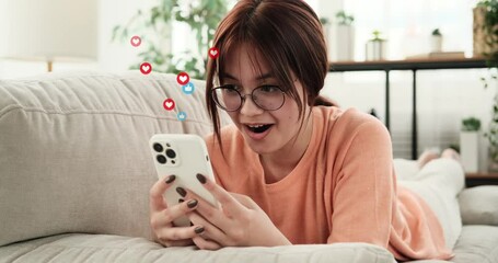 Surprised Caucasian teenager girl lying on sofa and using mobile phone for texting, messaging in social media app. Flying like icons. - Powered by Adobe