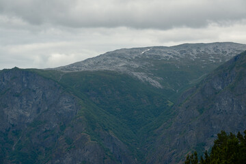 Naklejka premium Nature view of Norwegian mountains with white snow cover on its high ground from stegastein viewpoint on a cloudy summer day. Blue uv radiation on the mountains.